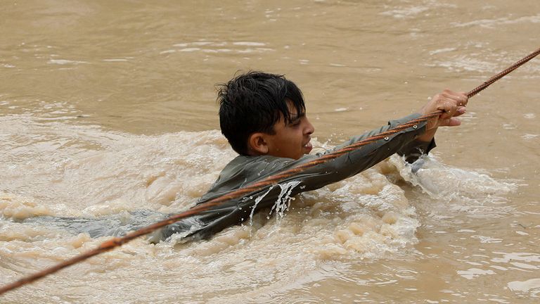 A boy crosses a flooded street, with the help of a wire fastened on both ends, following rains and floods during the monsoon season in Charsadda, Pakistan August 27, 2022. REUTERS/Fayaz Aziz