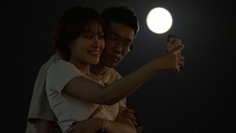 A couple poses for selfies with a Supermoon in the night sky in Beijing, Thursday, Aug. 11, 2022. (AP Photo/Ng Han Guan)