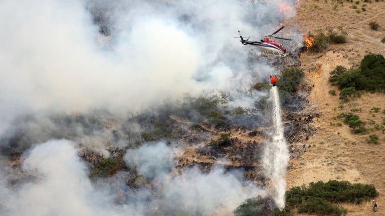 Firefighters battle a wildfire from the ground as a helicopter drops water above them in Springville on Monday, Aug. 1, 2022. The fire started when a man tried to burn a spider with a lighter. (Kristin Murphy/The Deseret News via AP)