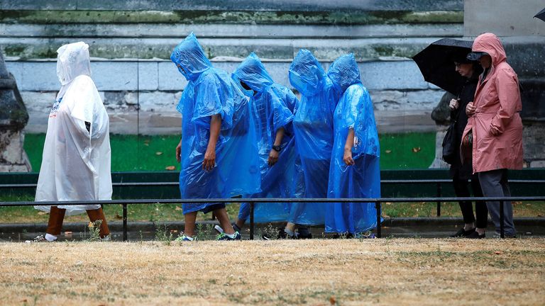 Visitors to Westminster Abbey protect themselves from a downpour of rain, in London, Britain, August 16, 2022. REUTERS/Peter Nicholls
