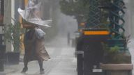 A woman makes her way through the strong wind and rain in Miyazaki, southern Japan, Sunday, Sept. 18, 2022, as a powerful typhoon pounded southern Japan. (Kyodo News via AP)