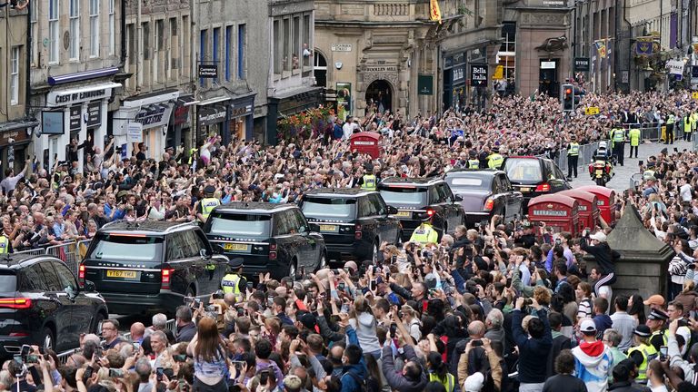 Crowds watch as the hearse carrying the coffin of Queen Elizabeth II, draped with the Royal Standard of Scotland, passes Mercat Cross in Edinburgh, Sunday, Sept. 11, 2022, as it continues its journey to the Palace of Holyroodhouse from Balmoral. (Ian Forsyth/Pool Photo via AP)