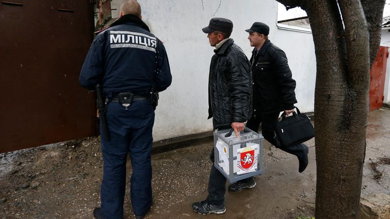 Election officials, accompanied by a police officer (L), arrive at a house with a mobile ballot box during a referendum in Crimea March 2014