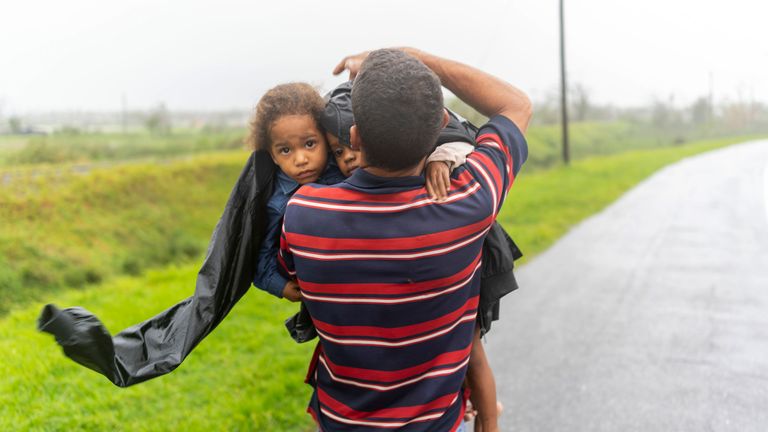 A man carries two children in the rain in search of shelter after Hurricane Ian flooded their home in Pinar del Rio, Cuba (AP Photo/Ramon Espinosa)