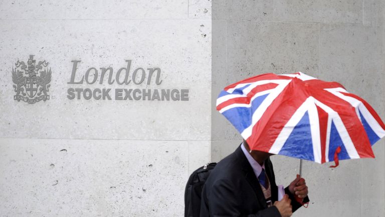 A worker shelters from the rain under a Union Flag umbrella as he passes the London Stock Exchange in London, Britain, October 1, 2008. REUTERS/Toby Melville/File Photo