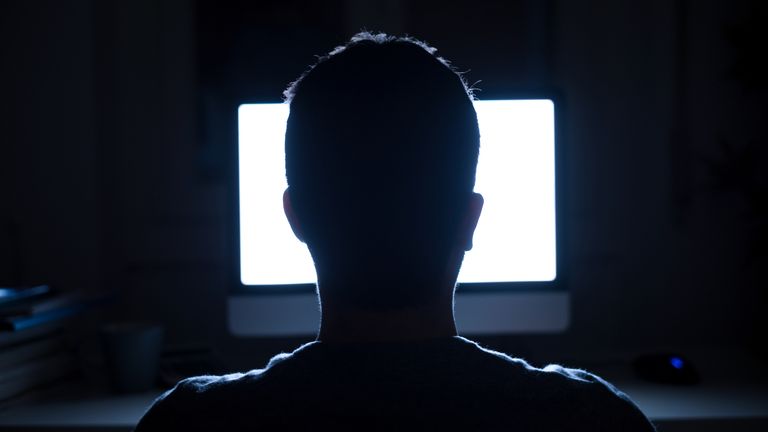 Silhouette of man&#39;s head in front of computer monitor light at night