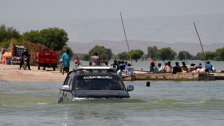 A vehicle travels amid floodwaters with boats in the background, following rains and floods during the monsoon season in Bajara village, Sehwan, Pakistan, August 31, 2022. REUTERS/Yasir Rajput NO RESALES. NO ARCHIVES.
