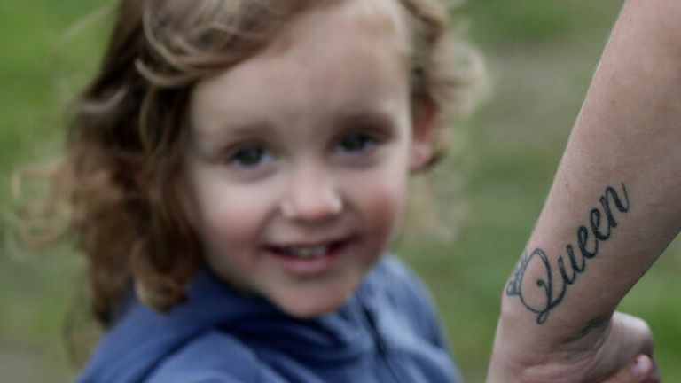 A child clutches her father&#39;s hand while watching the state funeral on a screen in Hyde Park. Her father has a permanent reminder of the Queen&#39;s years of sacrifice inked on his arm