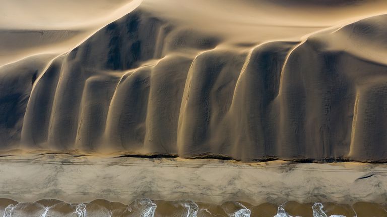 Siena Awards: Drone Photo Awards 2022. 
NATURE: 1st classified – Meeting - by David Rouge
This picture is the result of a dream come true: the meeting of the desert and the ocean. As the drone climbed higher, the photographer noticed a particular atmosphere, where the light highlighted the delicious shapes of these dunes flowing into the South Atlantic Ocean.
