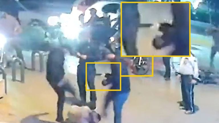 A man is being kicked by Iranian security forces in civilian clothes, one of whom is holding a gun