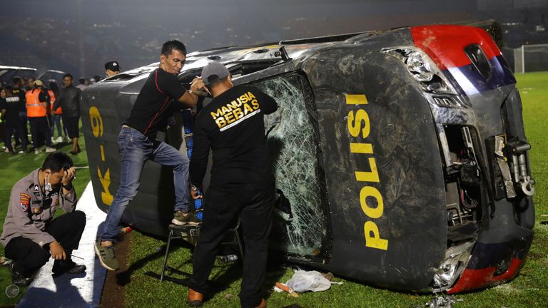 Officers examine a damaged police vehicle following a clash between supporters of two Indonesian soccer teams at Kanjuruhan Stadium in Malang, East Java, Indonesia, Saturday, Oct. 1, 2022. Clashes between supporters of two Indonesian soccer teams in East Java province killed over 100 fans and a number of police officers, mostly trampled to death, police said Sunday. (AP Photo/Yudha Prabowo)
