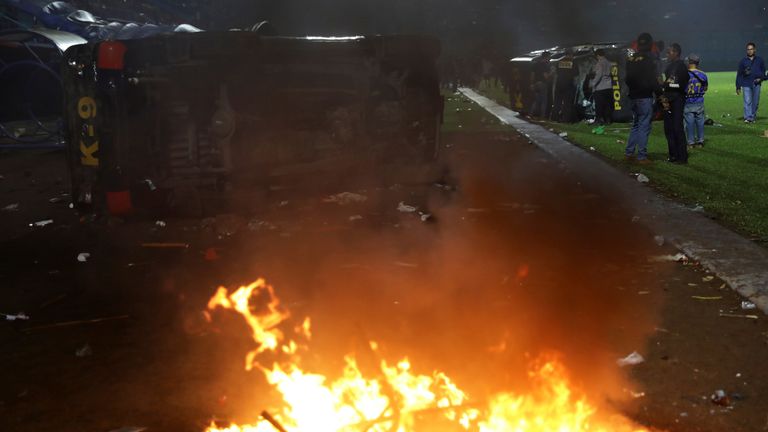 Plain-clothed officers stand near the wreckage of police vehicles damaged during a clash between supporters of two Indonesian soccer teams at Kanjuruhan Stadium in Malang, East Java, Indonesia, Saturday, Oct. 1, 2022. TClashes between supporters of two Indonesian soccer teams in East Java province killed over 100 fans and a number of police officers, mostly trampled to death, police said Sunday. (AP Photo/Yudha Prabowo)