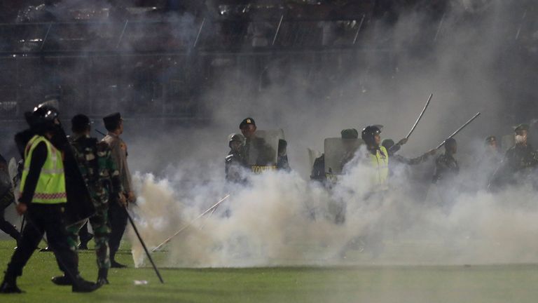 Police officers and soldiers stand amid tear gas smoke during a soccer match at Kanjuruhan Stadium in Malang, East Java, Indonesia, Saturday, Oct. 1, 2022. Clashes between supporters of two Indonesian soccer teams in East Java province killed over 100 fans and a number of police officers, mostly trampled to death, police said Sunday. (AP Photo/Yudha Prabowo)
