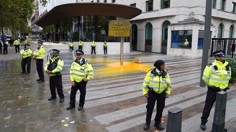 Police officers surround a sign which was spray painted by a Just Stop Oil protester outside New Scotland Yard in London. Picture date: Friday October 14, 2022.