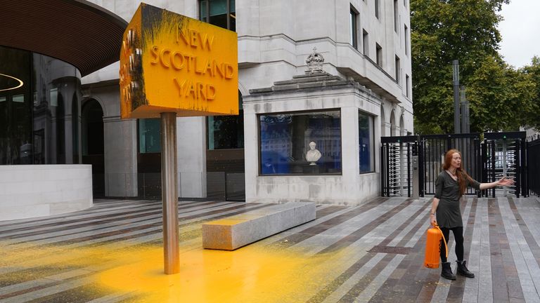A Just Stop Oil protester stands next to a sign she spray painted outside New Scotland Yard in London. Picture date: Friday October 14, 2022.