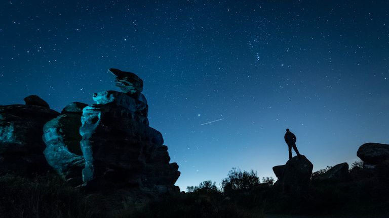 A plane passes by as a man stargazes at Brimham Rocks in Yorkshire as the Orionid meteor shower reaches its peak.