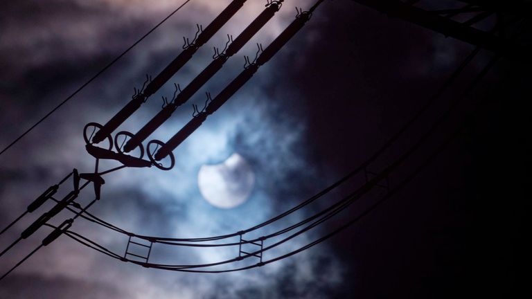 The sun, obscured by the moon, shines through the clouds. Insulators for high voltage power lines can be seen in the foreground. Photo by Henning Kaiser/picture-alliance/dpa/AP Images