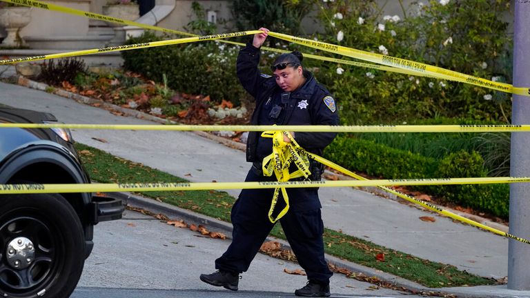 A police officer spreads more yellow tape on the closed road below Nancy and Paul Pelosi's house