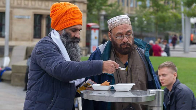 Volunteer feeding langar to a man with no arms.