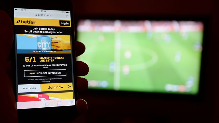 A smartphone user accesses the Betfair gambling website while watching a football match on television.