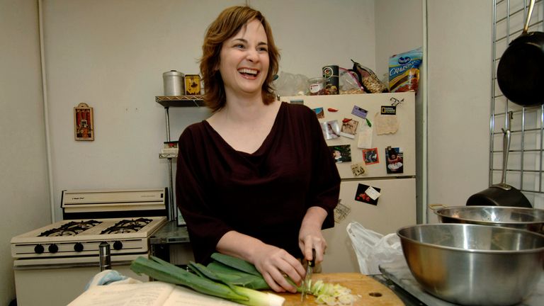 FILE - Food writer Julie Powell chops leeks to make potato leek soup, one of the first recipes in Julia Child's "Mastering the Art of French Cooking," shown at left, in her apartment in New York on Sept. 30, 2005. Powell, who became an internet darling after blogging for a year about making every recipe in Child...s book, leading to a book deal and a film adaptation, died of cardiac arrest on Oct. 26, 2022, at her home in upstate New York. She was 49. (AP Photo/Henny Ray Abrams, File)