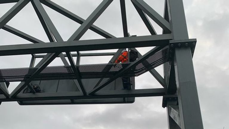 Handout photo taken with permission from the twitter account @SurreyPolice of a Just Stop Oil protester who has climbed a gantry on the M25 between junctions six and seven in Surrey, leading to the closure of the motorway. Surrey Police said the decision was made to close the road "for the safety of everyone" while officers attempt to remove the activist. Picture date: Monday November 7, 2022.