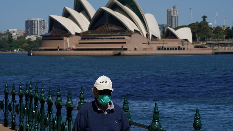 A man in a mask walks near the Sydney Opera House