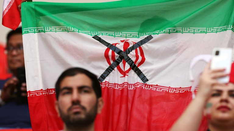 An Iranian flag is held up inside the stadium with a black cross across the national emblem