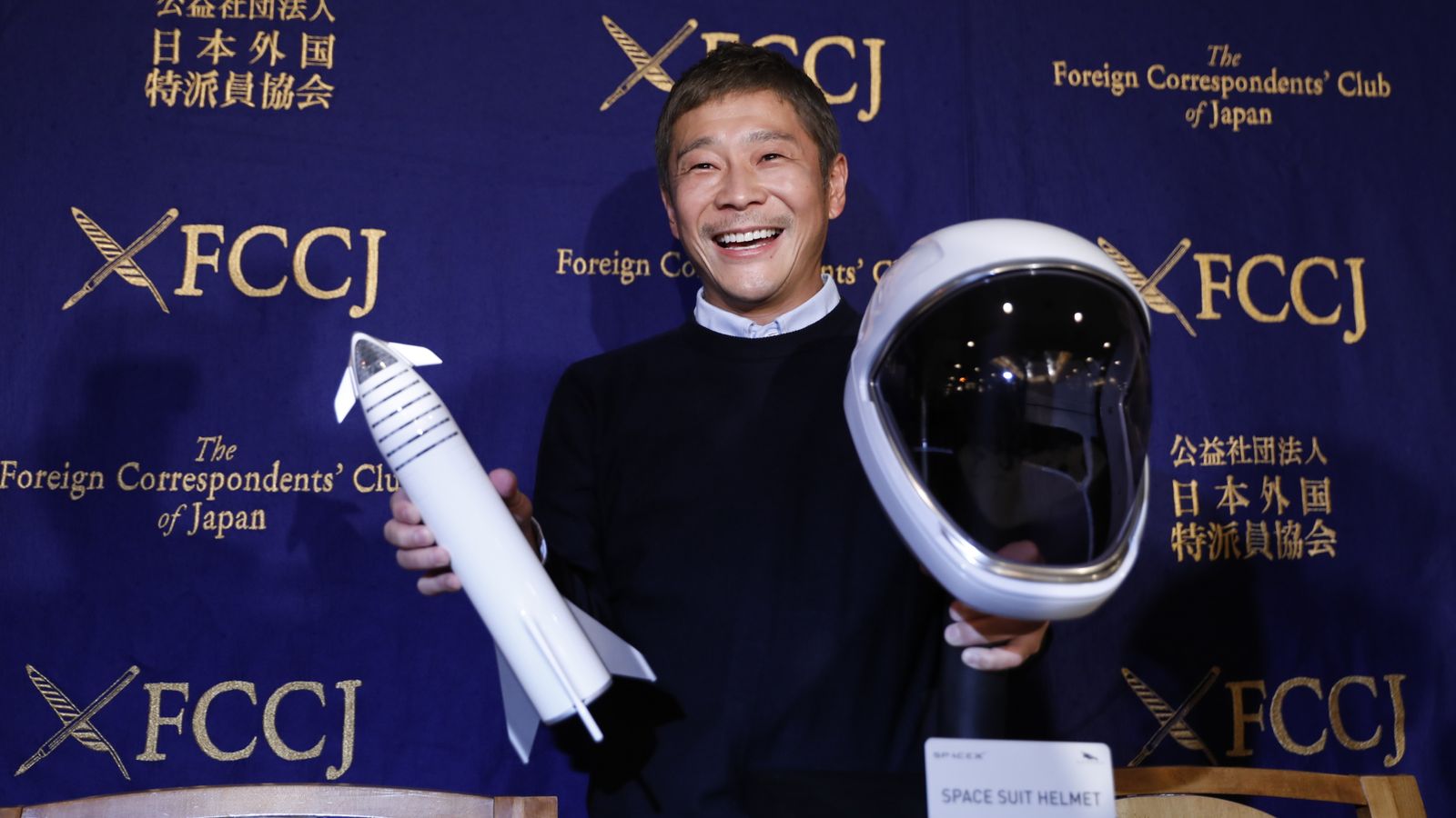 Yusaku Maezawa with models of the spacecraft and the crew's suit