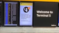 People stand near an arrivals board which displays a message warning users of terminal 5 about industrial action by Border Force staff, at Heathrow Airport