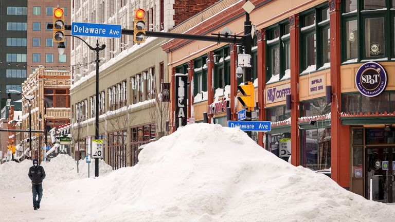 A man walks beside snow piles formed by plows following a winter storm in Buffalo, New York, U.S., December 27, 2022.  REUTERS/Lindsay DeDario