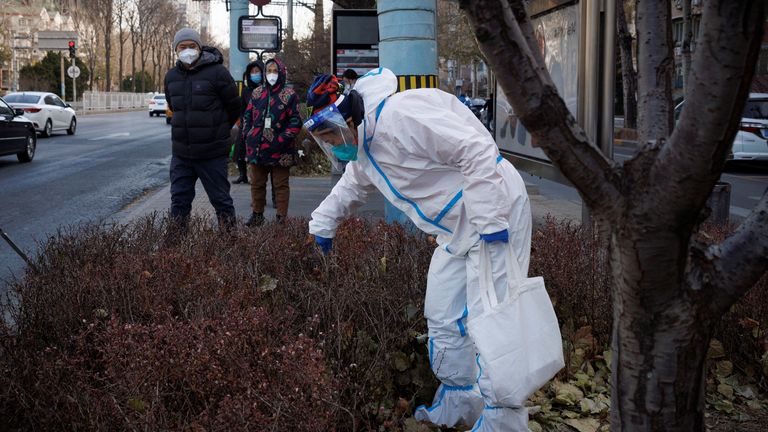 A street cleaner wears a protective suit as she picks up litter next to a bus stop in Beijing