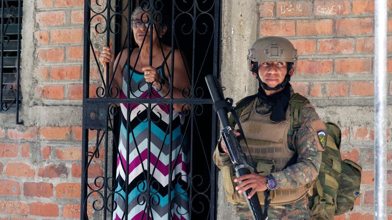 A resident looks out from her doorway as a soldier takes part in an operation in search of gang members