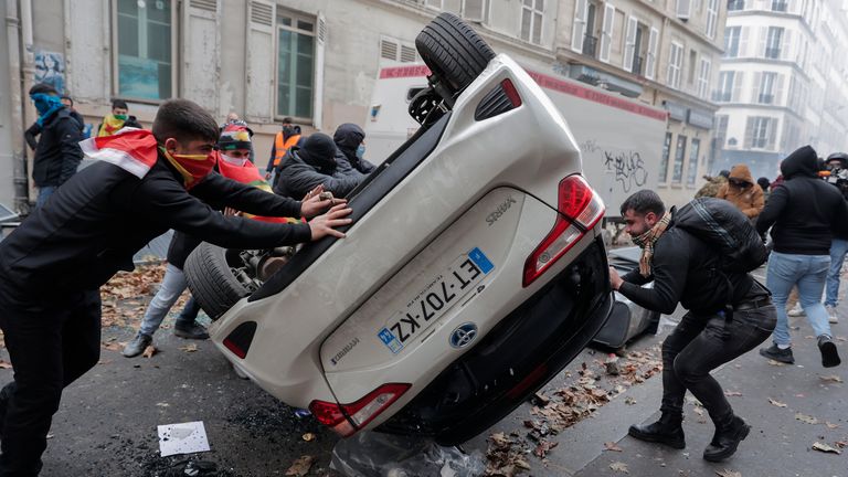 Demonstrators turn over a car during a protest against the recent shooting at the Kurdish culture center in Paris, Saturday, Dec. 24, 2022. Kurdish activists, left-wing politicians and anti-racism groups are holding a protest Saturday in Paris after three people were killed at a Kurdish cultural center in an attack aimed at foreigners.(AP Photo/Lewis Joly)