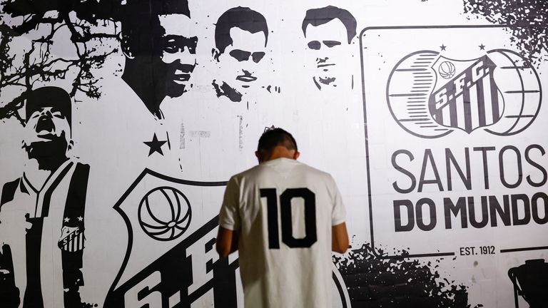 A man stands in front of a portrait of Brazilian soccer legend Pele as people gather to mourn his death on December 29, 2022 in Santos, Brazil.  REUTERS/Amanda Perobelli