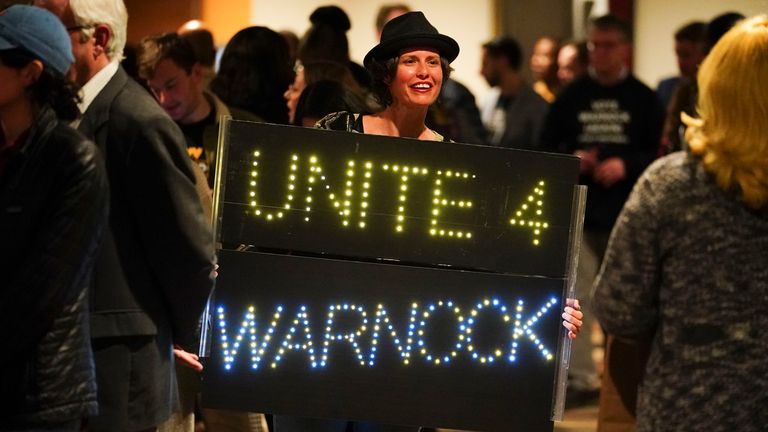 Athena Soules walks with a sign in the hall during an election night watch party for Democratic Sen. Raphael Warnock, Tuesday, Dec. 6, 2022, in Atlanta. Georgia voters are deciding the final Senate contest in the country, choosing between Democratic Sen. Raphael Warnock and Republican candidate Herschel Walker. (AP Photo/John Bazemore)