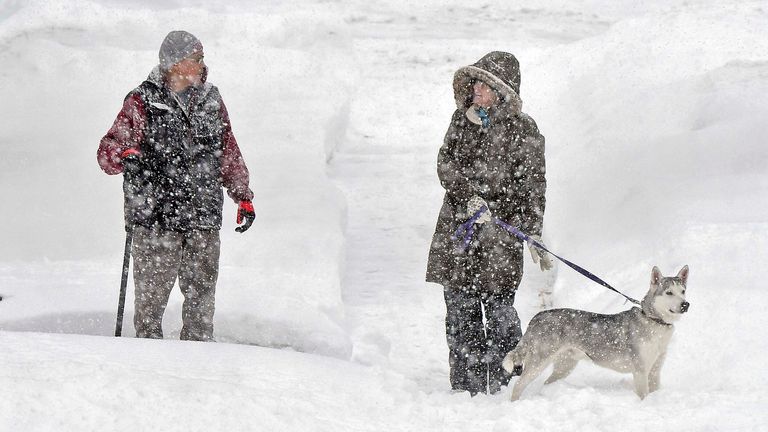 Gordon Weyaus, left, and Katy Little with dog Jax walk along Mandan Street in Bismarck, N.D., in the snow on Wednesday, Dec. 14, 2022. (Tom Stromme/The Bismarck Tribune via AP)