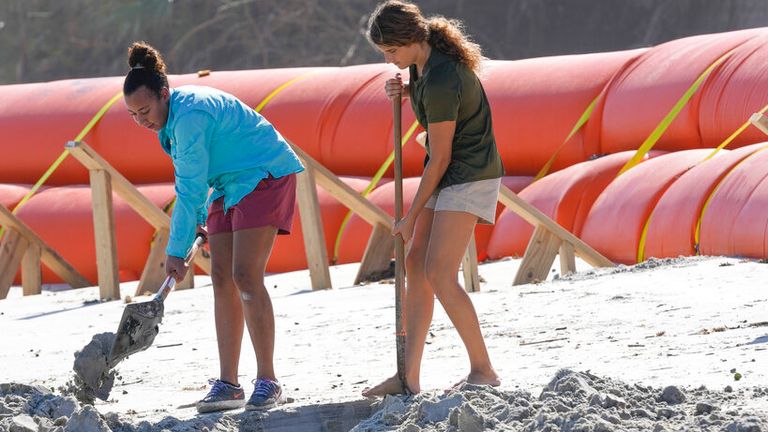 Suzzanna Rogers, left, and Olivia Storkamp, volunteers working with archaeologists, dig in the sand exposing part of a wooden structure on the shore, Tuesday, Dec. 6, 2022, in Daytona Beach Shores