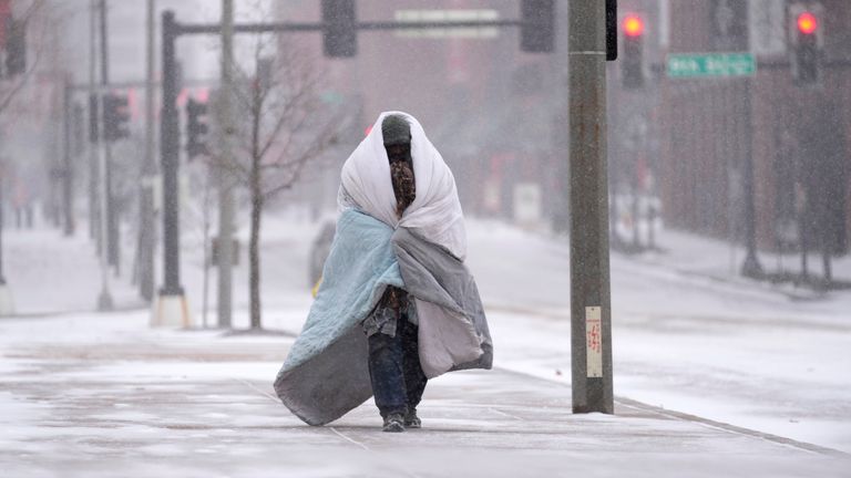 A person wrapped in a blanket walks on a sidewalk as snow begins to fall in St. Louis PIC:AP