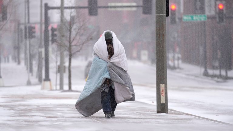 A person wrapped in a blanket walks on a sidewalk as snow begins to fall  in St. Louis
PIC:AP