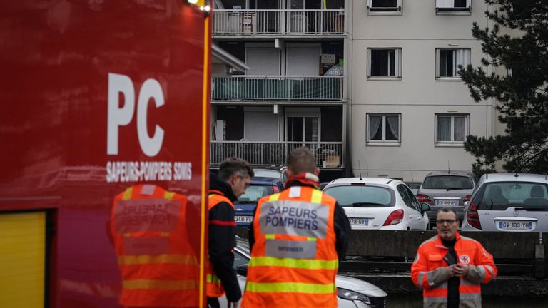 Firefighters stand next to apartment buildings seen in background, in Vaulx en Velin, outside Lyon, central France, Friday, Dec. 16, 2022. French authorities say 10 people including five children died in a fire in an apartment building outside the city of Lyon. The cause of the fire is being investigated. (AP Photo/Laurent Cipriani)