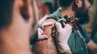 A tattoo artist tattooing a man&#39;s arm in his tattoo studio