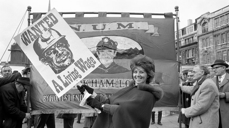 Snug in a cape, Mrs Margaret Dobb of Kirkby, Nottingham, brnadishes a placard in vicinity of the Tower of London, here today. Margaret is the wife of a miner from Bentinck Colliery, Nottinghamshire, the largest colliery in Europe. She is among miners, their wives and trades unionists who plan to march from Tower Green to Westminster this afternoon where they will lobby MP&#39;s at the House of Commons.
