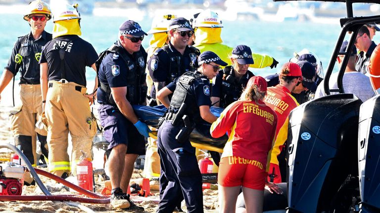 Rescuers remove a body from a helicopter crash scene near Seaworld, on Australia's Gold Coast, Monday, Jan. 2, 2023. Two helicopters collided, killing several passengers and seriously injuring a few others in a crash which attracted emergency help from bathers enjoying the water during the austral summer.  (Dave Hunt/AAP Image via AP)