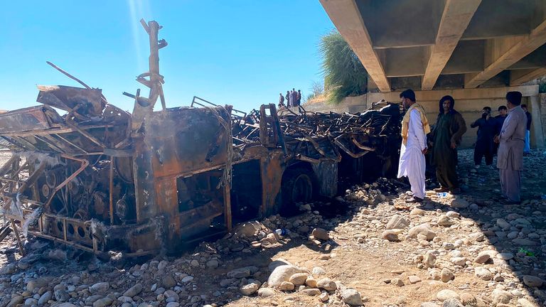 People look at the burnt wreckage of a bus accident in Bela, an area of Lasbela district of Balochistan province, Pakistan, Sunday, Jan. 29, 2023. The passenger bus crashed into a pillar and fell off a bridge, catching fire and killing dozens of people in southern Pakistan on Sunday, a government official said. (AP Photo/Muhammad Saleem)