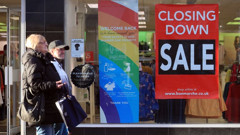 People walk past a shop with a closing down sale sign in the window