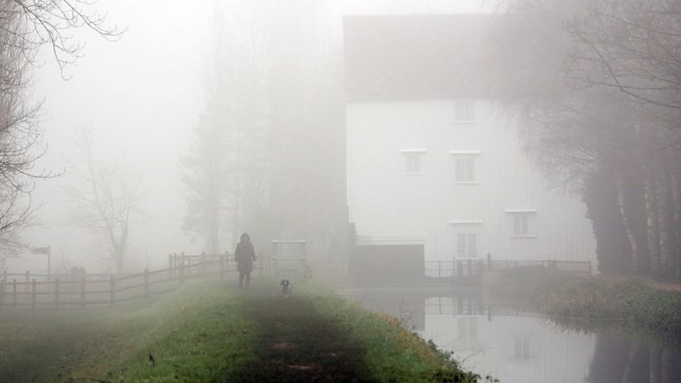 A woman walks a dog as fog lingers at Lode Mill in Cambridgeshire. File pic