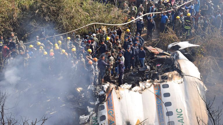 Nepalese rescue workers and civilians gather around the wreckage of the crashed airliner 