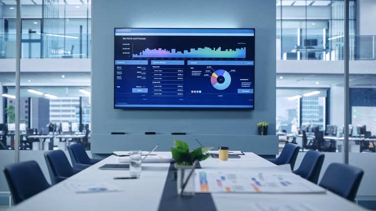 Modern Empty Meeting Room with Big Conference Table with Various Documents and Laptops on it, on the Wall Big TV with Big Data, Statistics, Talks about Company Growth. Contemporary Designed Workplace.