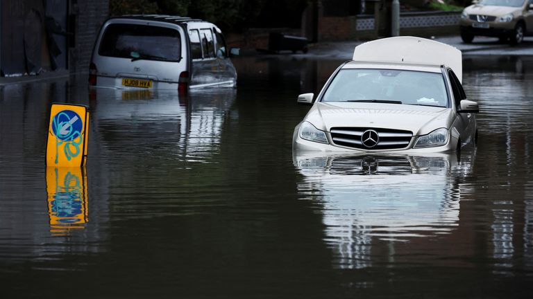 A car is left partially submerged in water after heavy rain flooded a section of road in Stockport
